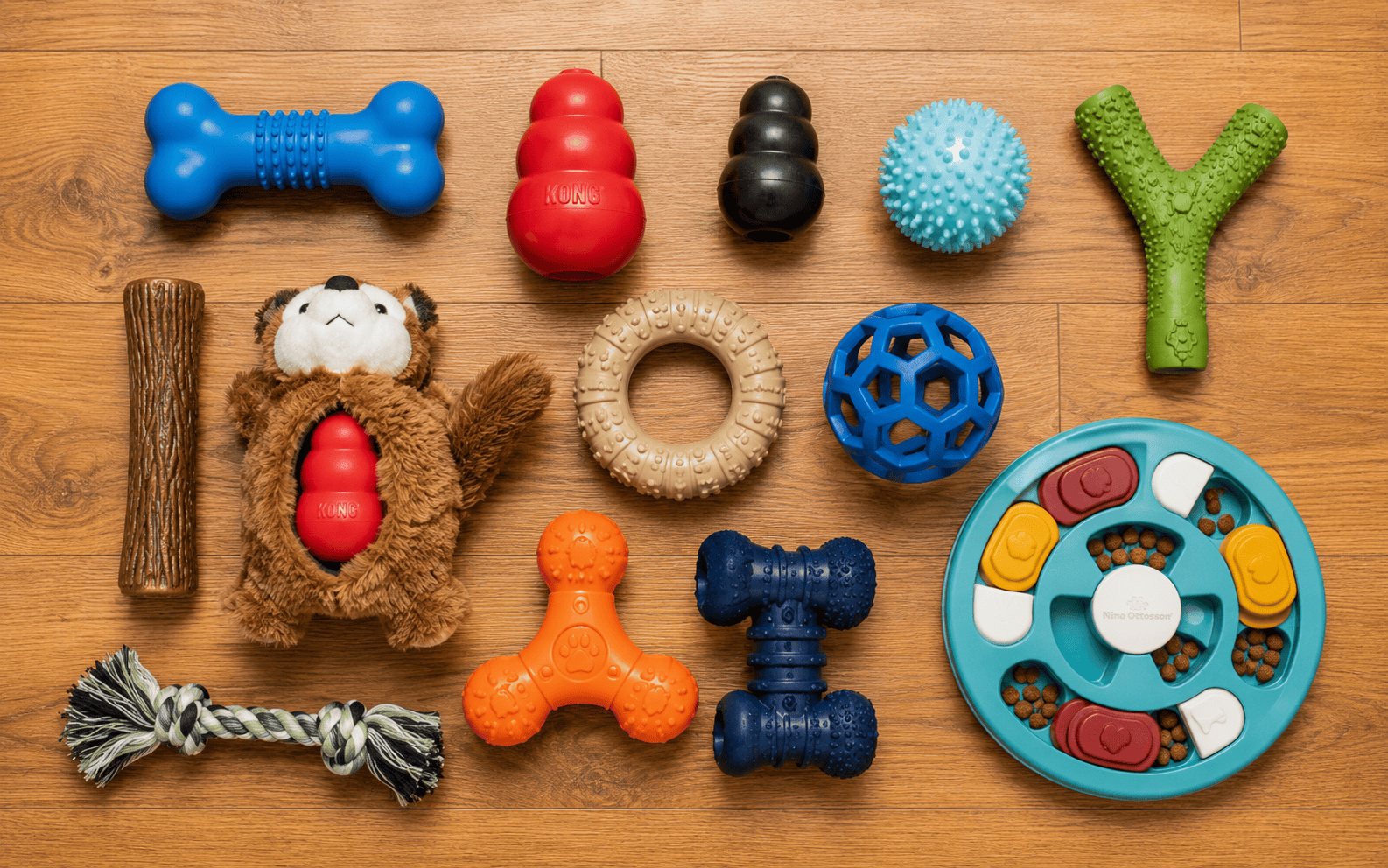 A selection of colorful dog toys and a treat puzzle are neatly displayed on a wooden floor.